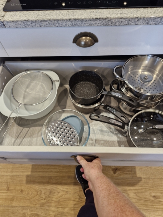 An open kitchen cupboard containing saucepans and cooking utensils