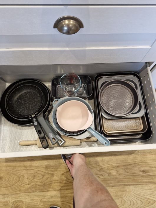 An open drawer containing baking tins and saucepans